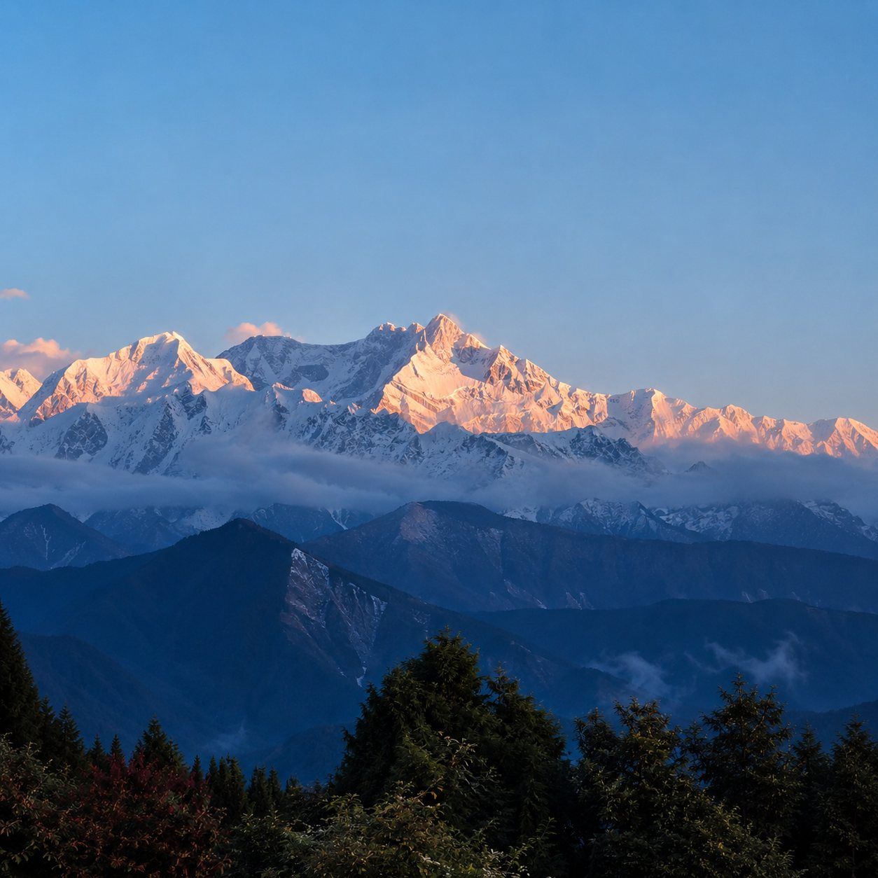 Dawn alpenglow on the Kanchenjunga range — open sky above golden peaks, with layered ridgelines, mist and forest below.
